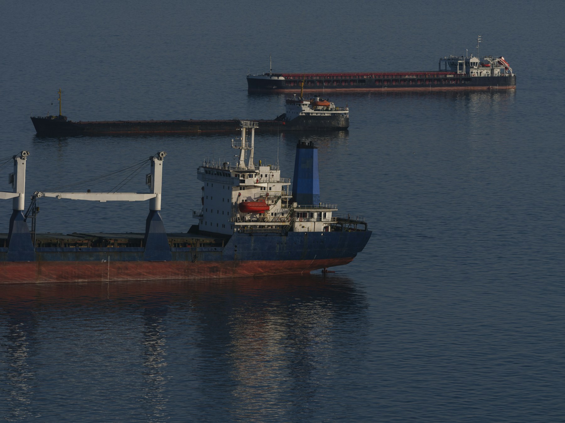 Three cargo ships at anchor on a calm, dark blue sea