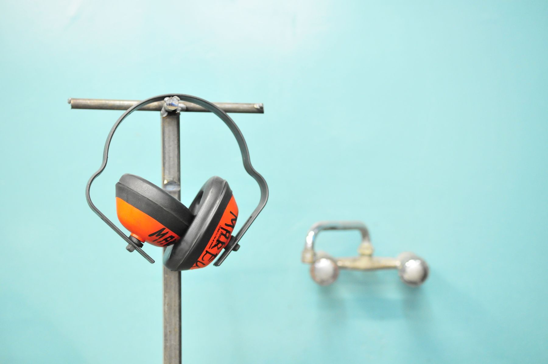 Orange ear defenders hanging on a stand against a teal wall