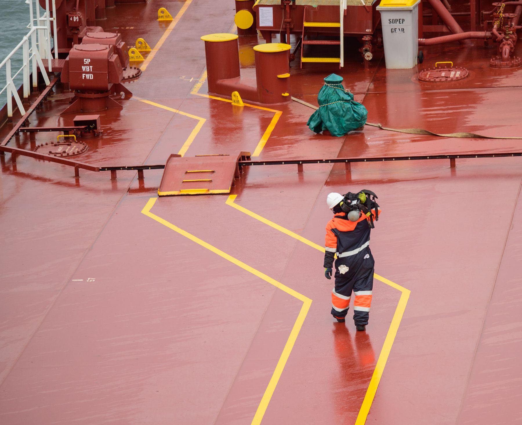 A crew member in protective gear walking across the red deck of a tanker