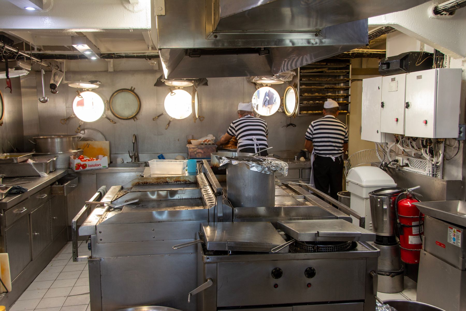 Two cooks preparing food in a ship's galley, seen from behind