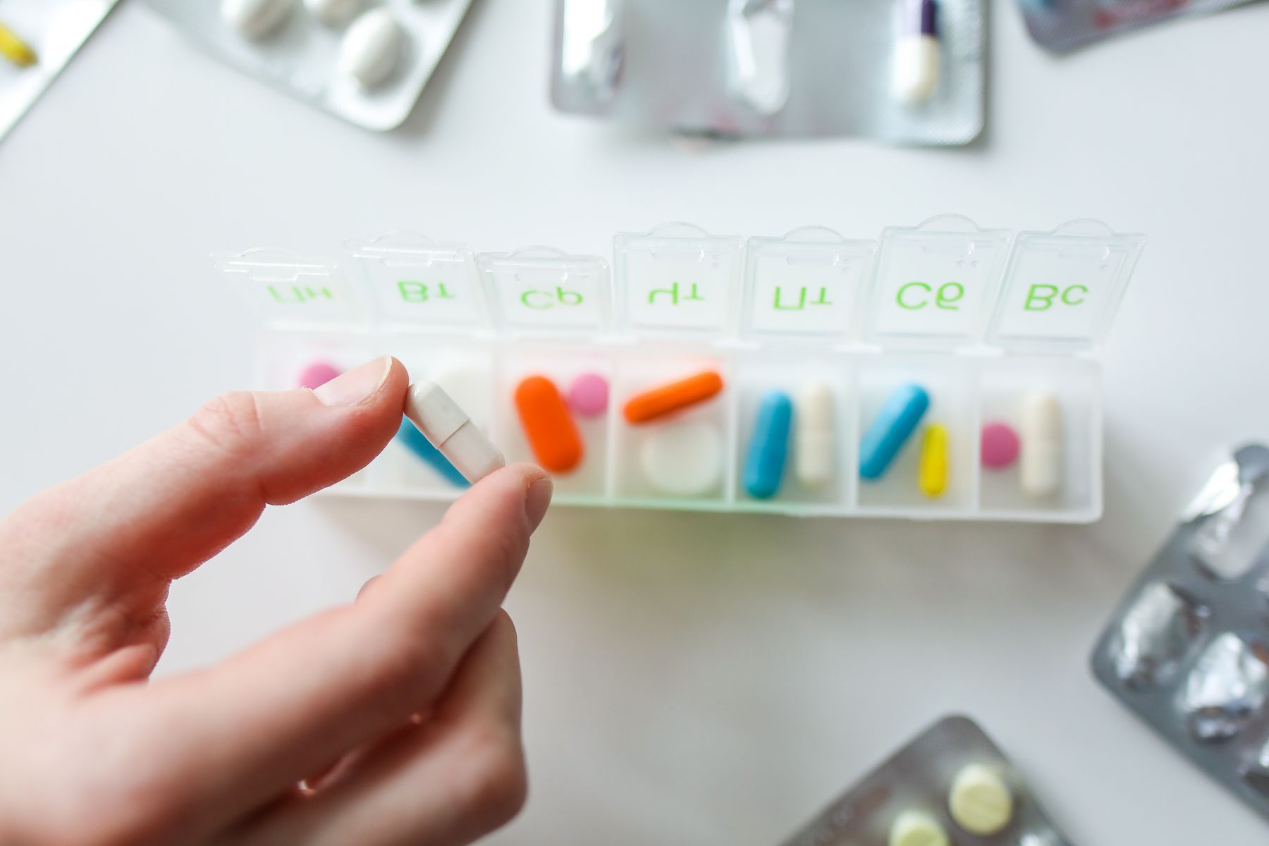 A hand taking a capsule from a weekly pill organiser