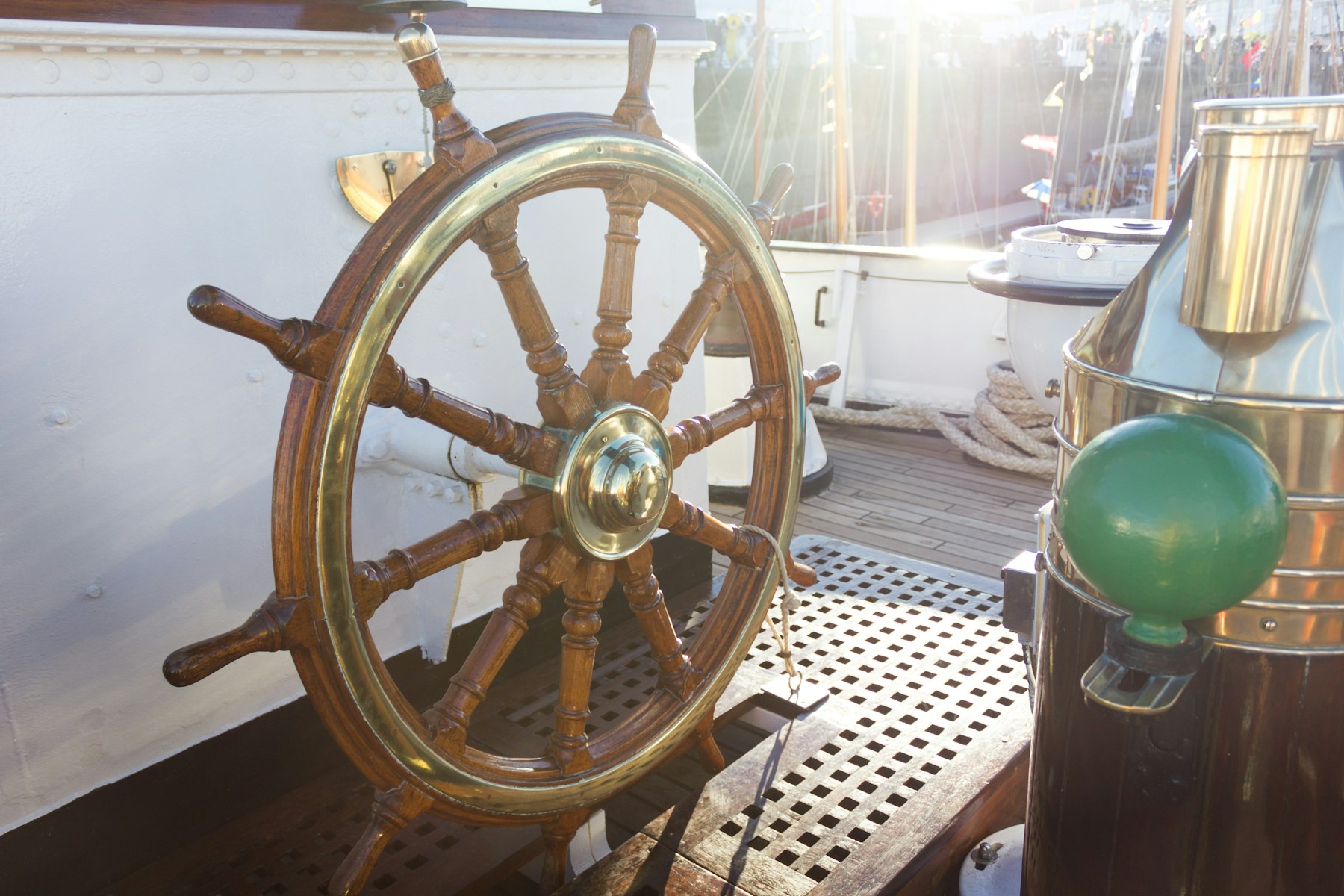 A brass ship's wheel on deck in the sunshine