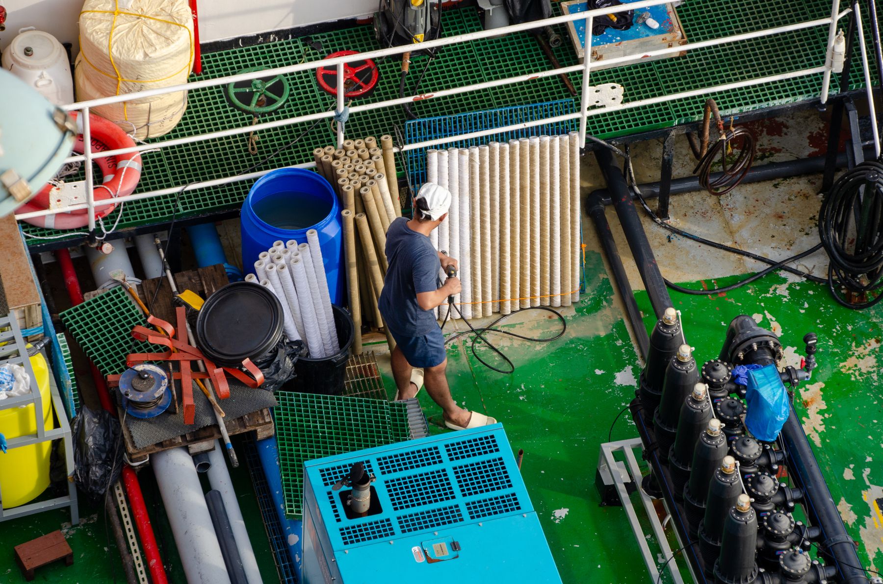 A crew member working among equipment and pipes on a ship's deck, seen from above