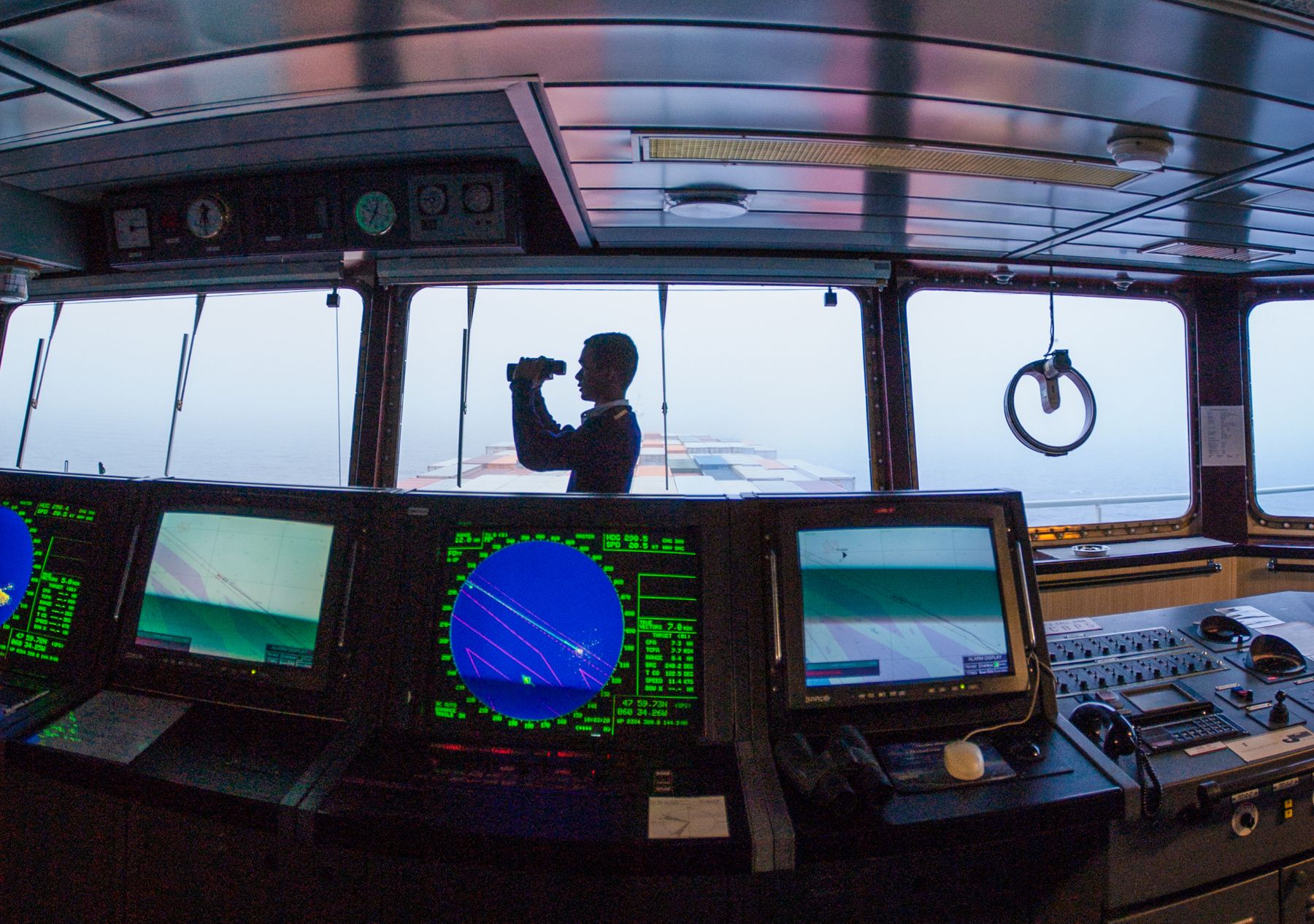 A navigator in silhouette using binoculars on a ship's bridge