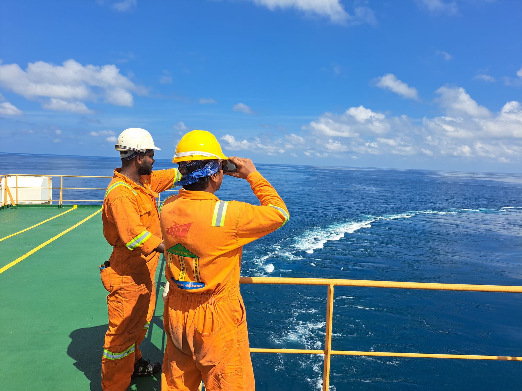 Two crew members in orange safety gear looking out to sea from a ship's deck
