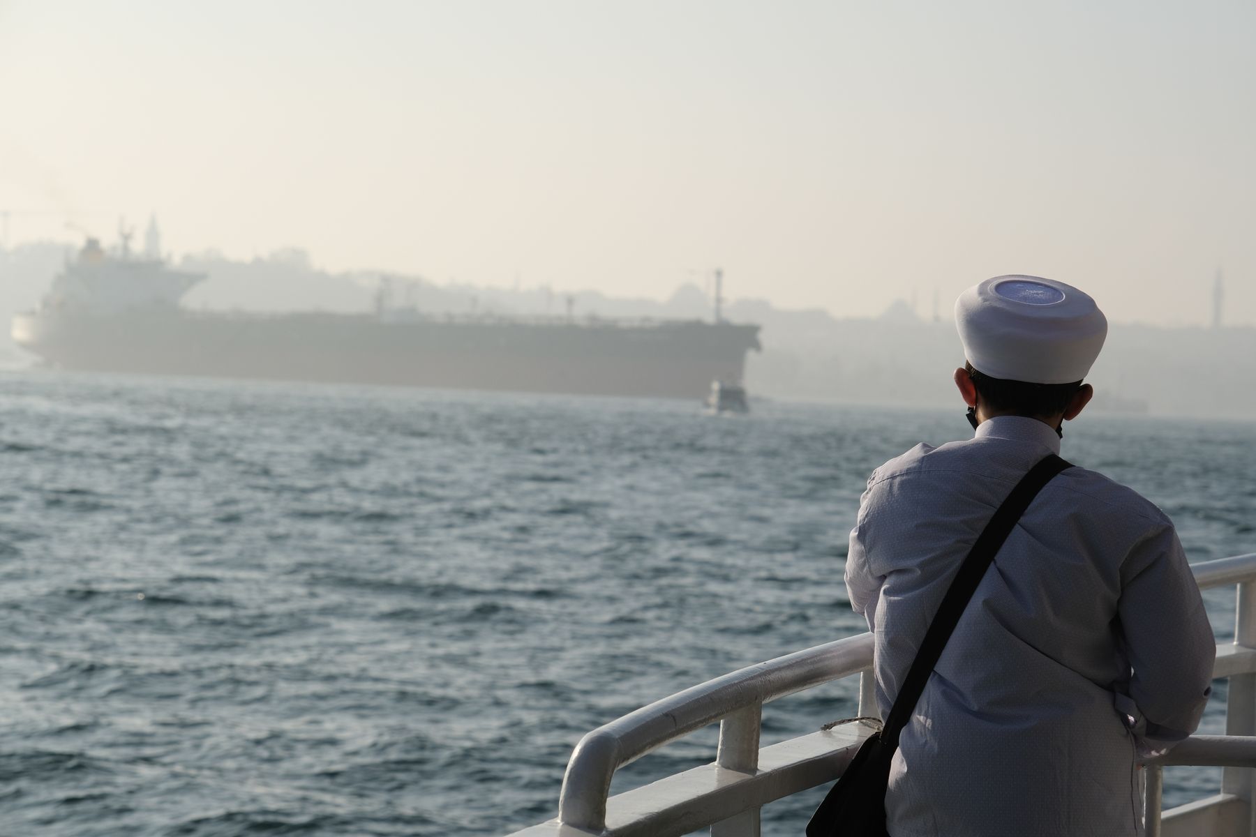 A sailor on deck watching a tanker in misty water, seen from behind