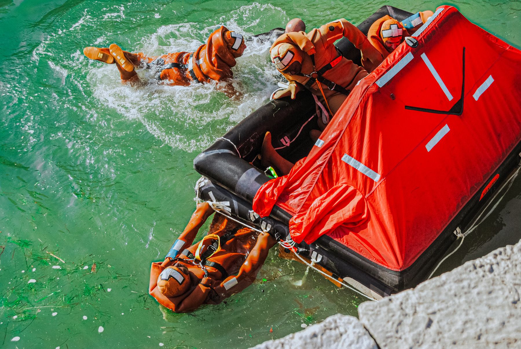 A team in orange survival suits practising with a life raft