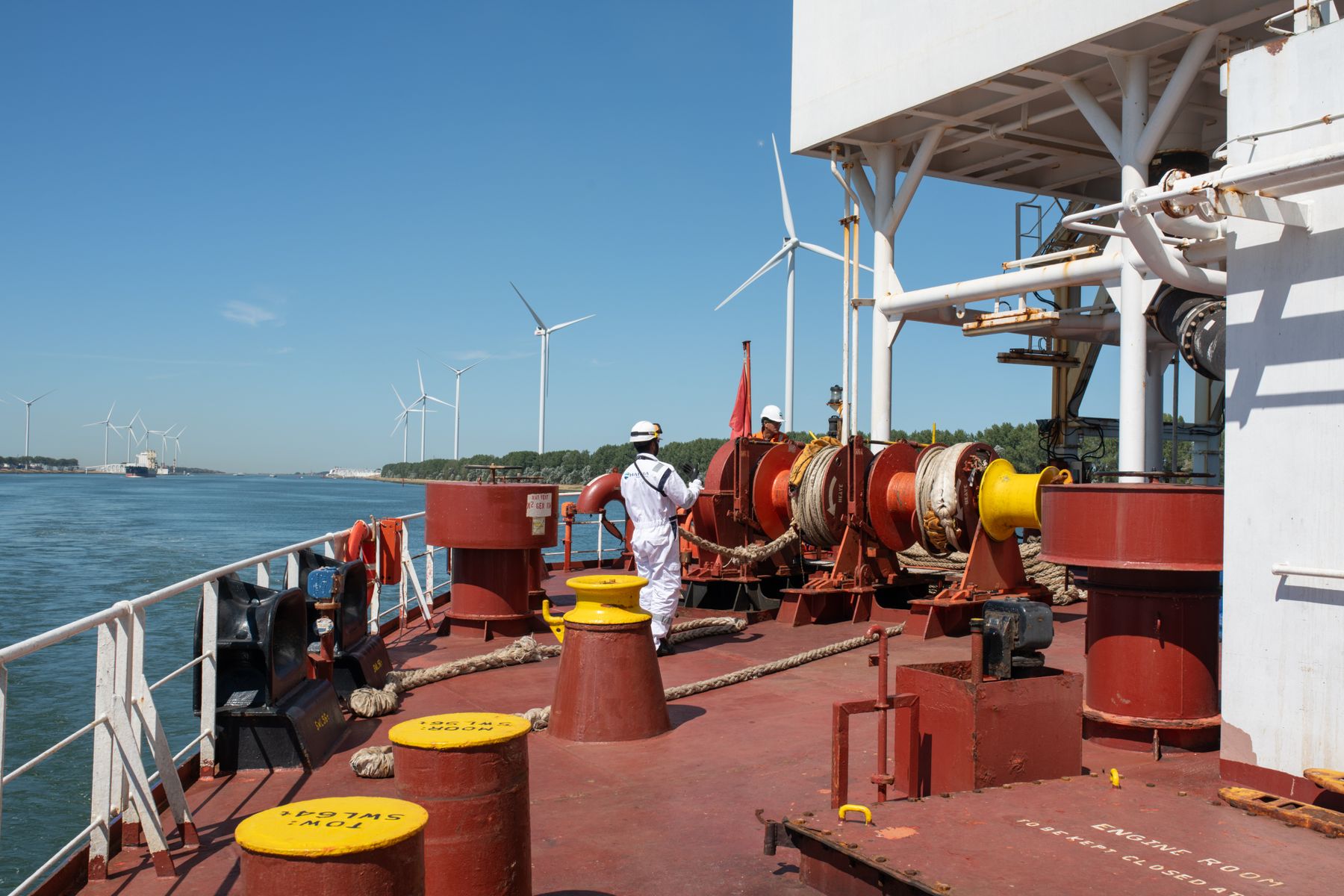 A crew member working on deck with offshore wind turbines in the distance